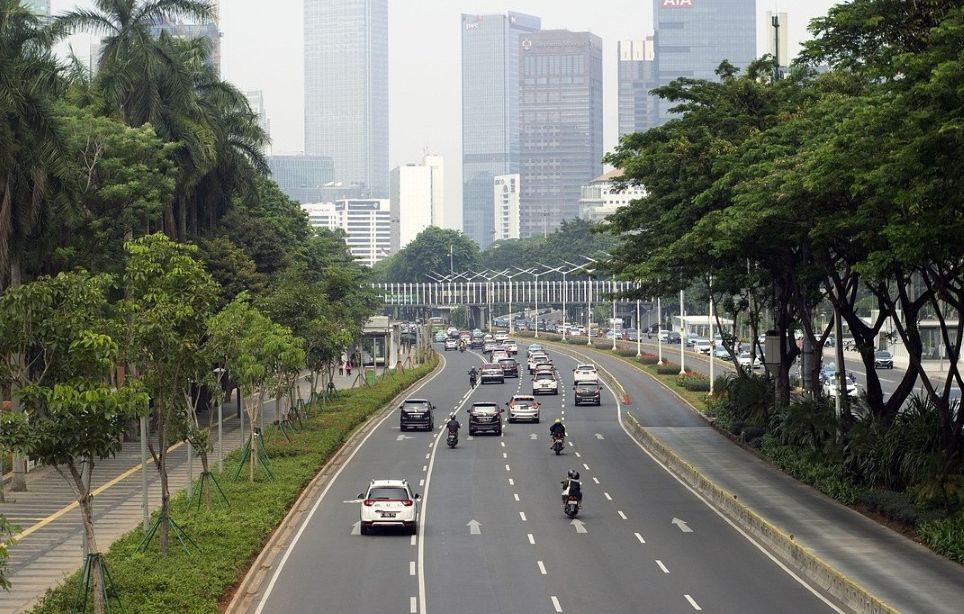 Pemandangan jalan raya perkotaan dengan jalur hijau, pepohonan, dan gedung tinggi, simbol integrasi ruang terbuka hijau dalam tata kota modern