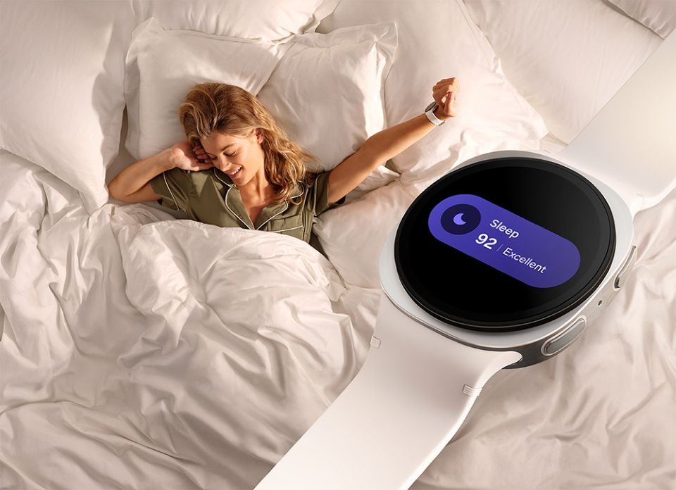 Perempuan berbaring di tempat tidur dengan smartwatch Galaxy Watch 8 yang menampilkan skor tidur “Sleep 92 Excellent”